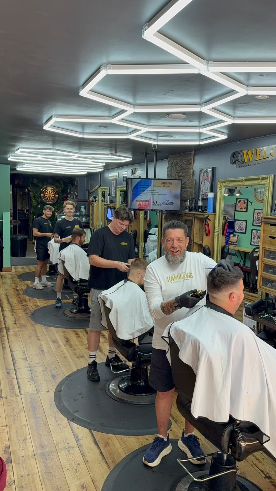 The Hamilton's team cutting hair at a busy shop floor in Redruth, with our team of experienced barbers at work under hexagon lighting