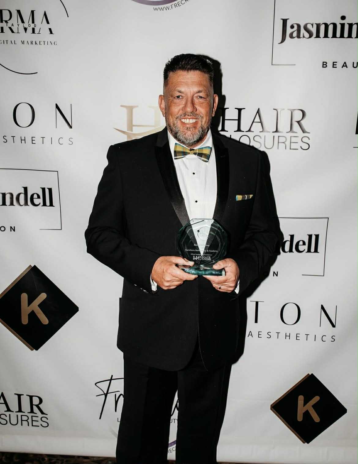 Liam Hamilton in black tie holding the Best Barbershop 2025 award at the awards evening