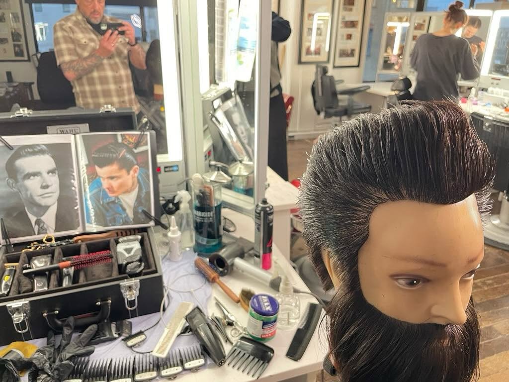 Period-barbering work displayed on a mannequin at the Christine Blundell Academy, with Liam reflected in the mirror
