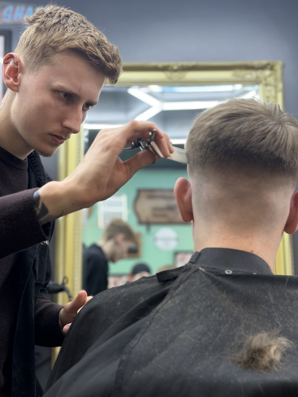A barber detailing a haircut seen in the barbershop mirror